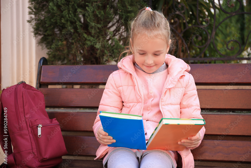 Cute little girl with backpack and books on bench outdoors Cute little girl with backpack and books on bench outdoors