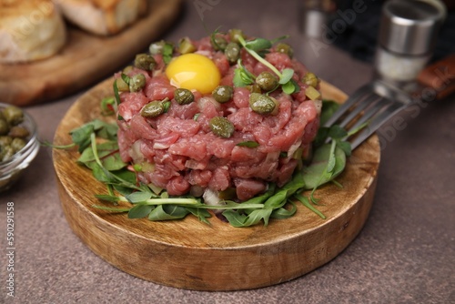 Tasty beef steak tartare served with yolk, capers and microgreens on brown table, closeup