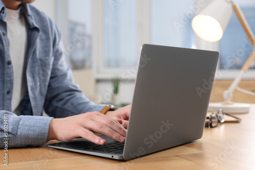 Man working on laptop at wooden desk indoors, closeup
