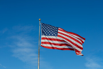 Close up view of an American flag waving on a flagpole, with blue sky background and copy space
