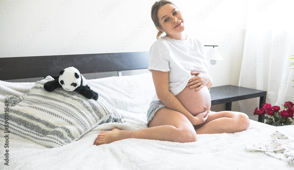 Pregnant woman sitting on a bed holding .The concept of pregnancy, motherhood and prenatal care. Mom with a new life. Pregnant woman sitting on a bed holding .The concept of pregnancy, motherhood and prenatal care. Mom with a new life.