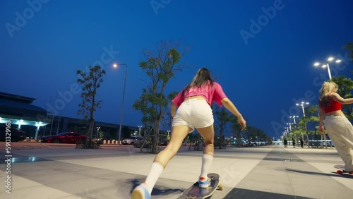 Cool Asian girl skating on longboard skate at park on summer holiday vacation. Stylish woman friends having fun urban outdoor active lifestyle practicing skateboarding together on city street at night photo