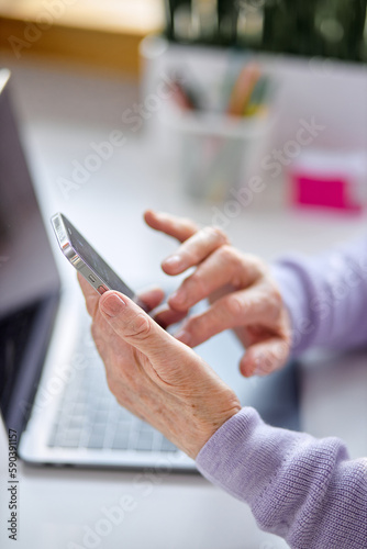 Cropped senior woman using smartphone checking email news online sitting in living room, searching for friends in internet social networks or working on computer, writing blog