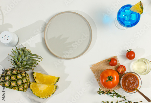 Fototapeta Naklejka Na Ścianę i Meble -  Top view shot of prop white dish with other ingredients aroma oil in glass vial, pineapple , tomato, sause , pepper bottle  on white table