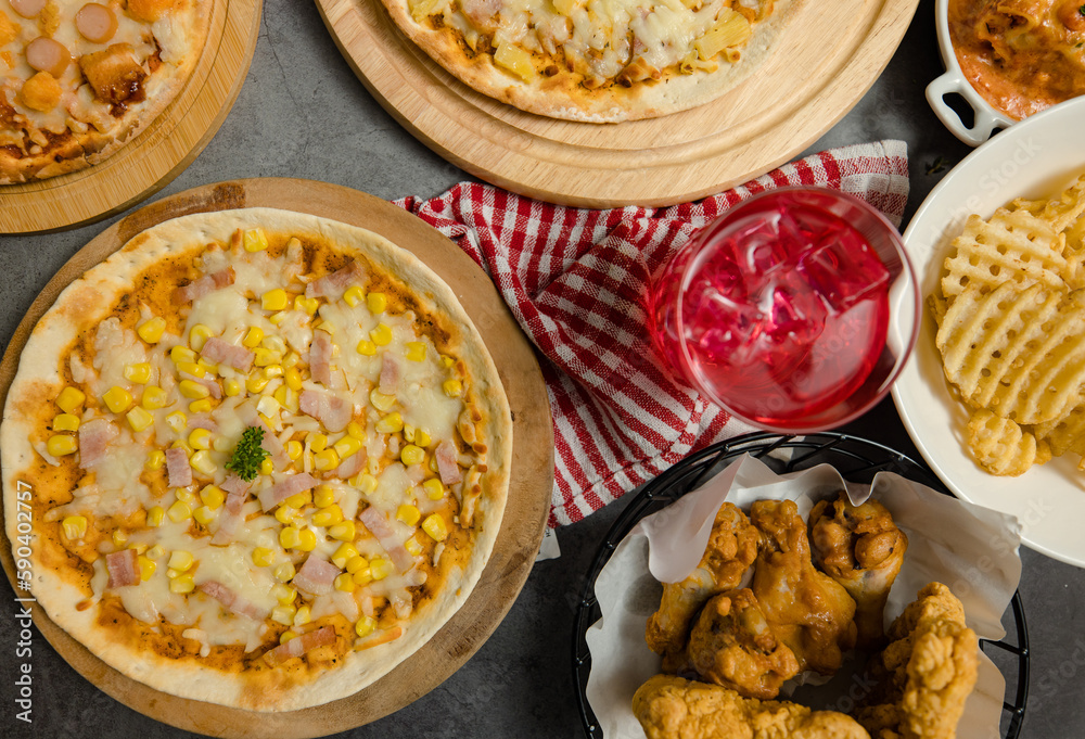 Top view shot of various kinds of delicious tasty juicy cheesy pizza placed on wooden board on party table around with other fast food for eating dinner together. Top view shot of various kinds of delicious tasty juicy cheesy pizza placed on wooden board on party table around with other fast food for eating dinner together.