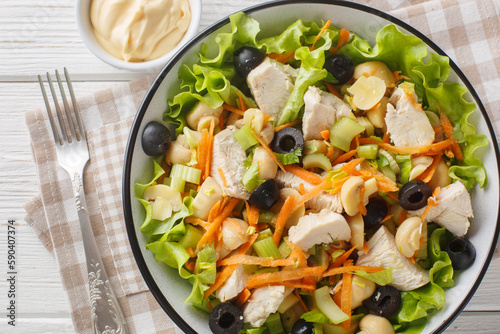 Healthy diet salad with chicken, mushrooms, carrots, celery, olives, cheese and lettuce close-up in a bowl on a wooden table. Horizontal top view from above
