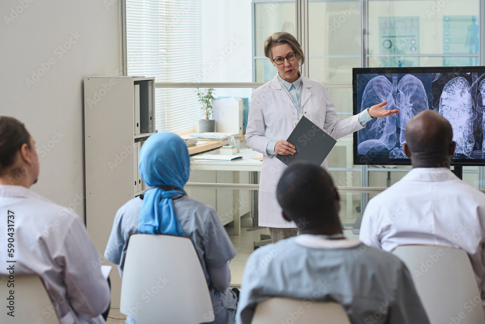 Female doctor pointing at monitor with x-ray image of lungs and discussing disease with her colleagues during conference Female doctor pointing at monitor with x-ray image of lungs and discussing disease with her colleagues during conference