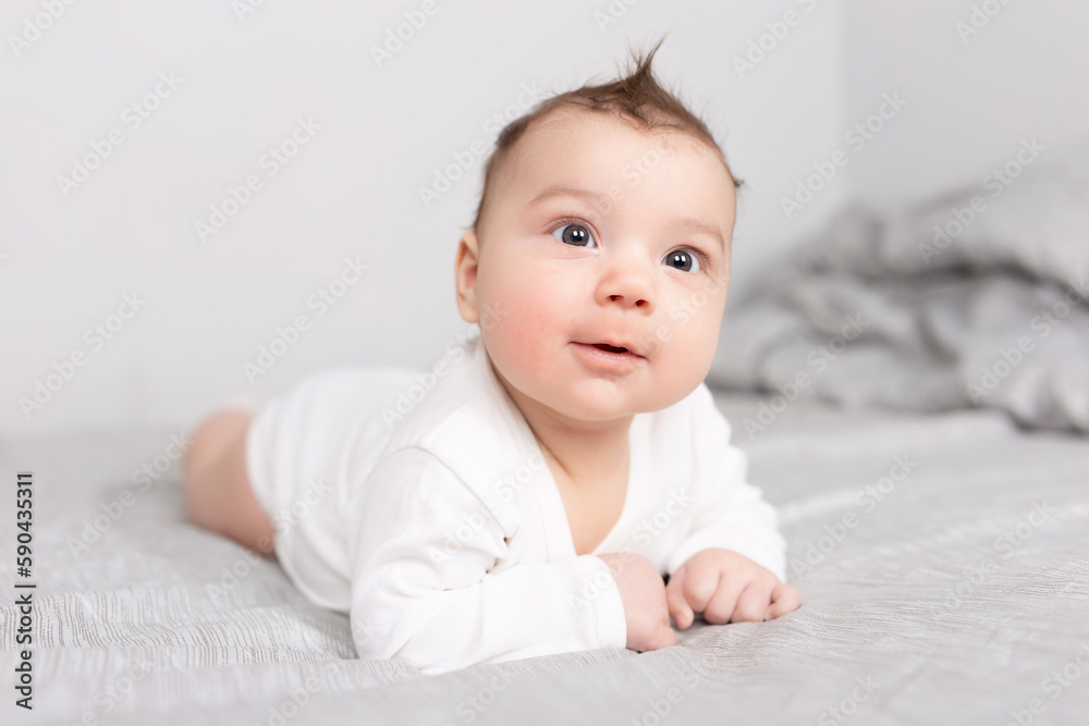 The baby lies on his stomach on the bed. A beautiful baby smiles. Mockup for advertising, design, celebration, postcards.