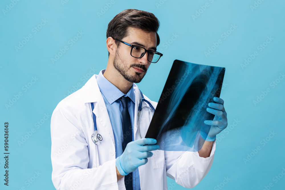 Male doctor in a white coat surgeon looks at an x-ray of a patient smile on a blue isolated background, copy space, space for text Male doctor in a white coat surgeon looks at an x-ray of a patient smile on a blue isolated background, copy space, space for text