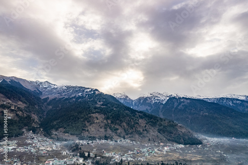 monsoon clouds moving over snow covered himalaya mountains with the blue orange sunset sunrise light with town of kullu manali valley at the base of mountains © Memories Over Mocha