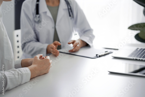 Doctor and patient discussing current health examination while sitting at the desk in clinic office. The focus is on female patient's hands, close up. Perfect medical service and medicine concept