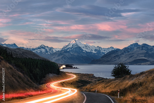 Road to Mt Cook in New Zealand during sunset. Traffic is causing light trails leading to the mountain. 