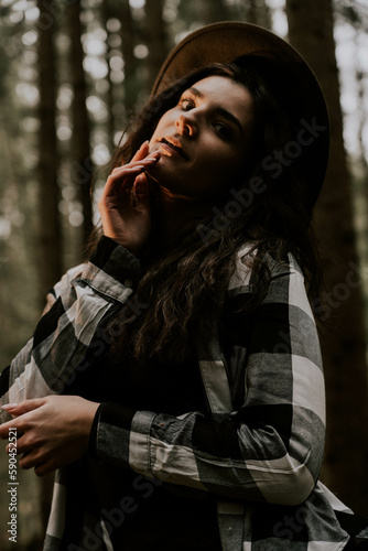 Stylish hipster girl in a hat wrapped in a checkered plaid posing in the base of a pine forest.Travel concept