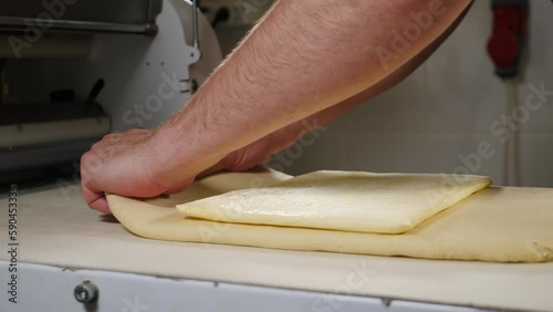 Bakery Manufacturing, food industry. Chef baker lays large piece of butter in puff pastry for making croissants. Dough processing. Confectioner rolls out dough on sheeter for making pies, buns. 4 k photo