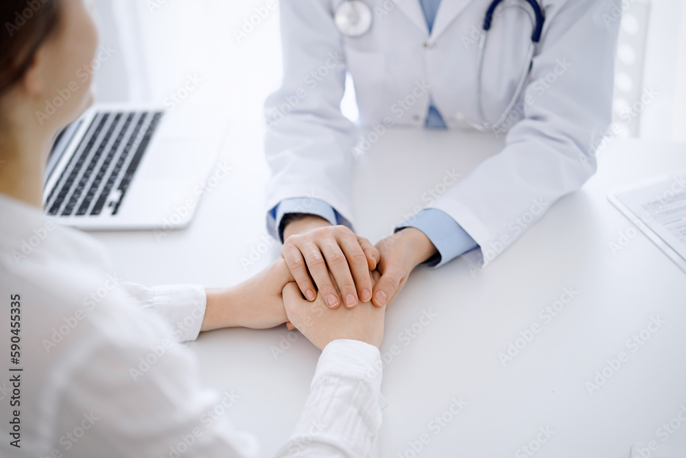 Doctor and patient sitting opposite each other at the table in clinic office. The focus is on female physician's hands reassuring woman, only hands, close up. Medicine concept Doctor and patient sitting opposite each other at the table in clinic office. The focus is on female physician's hands reassuring woman, only hands, close up. Medicine concept