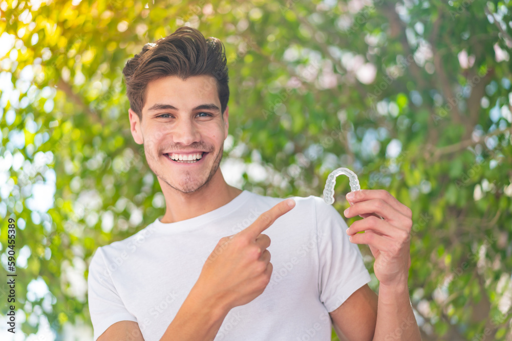 Young caucasian man holding invisible braces at outdoors and pointing it Young caucasian man holding invisible braces at outdoors and pointing it