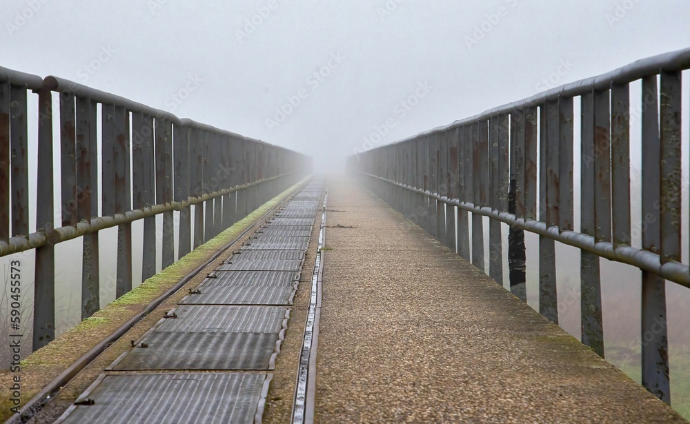 Landscape of a bridge with old metal rusty fences under a cloudy sky and sunlight