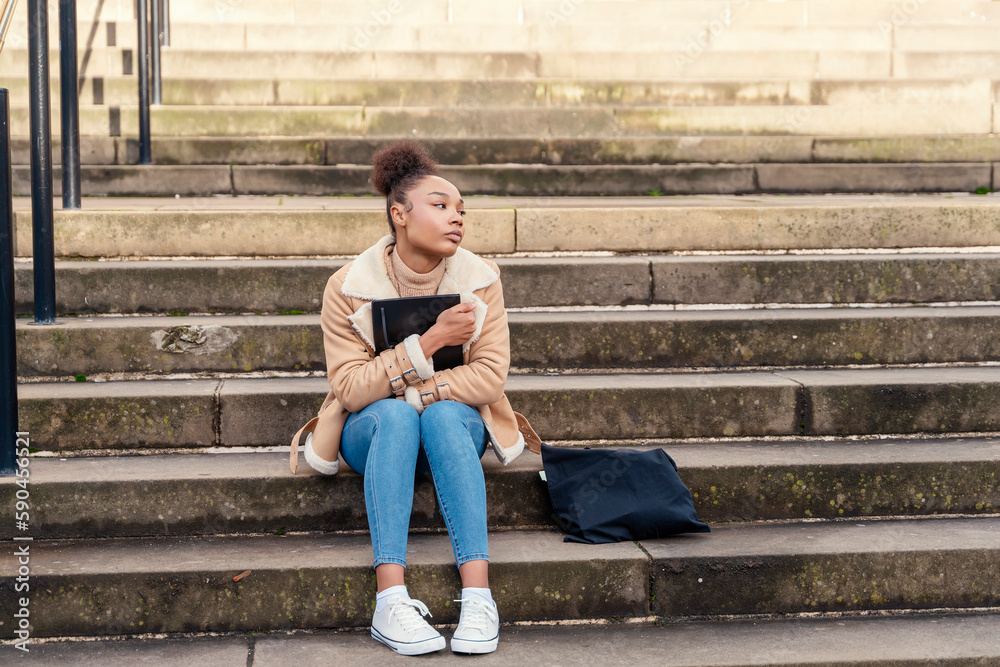 African Ethnicity woman  student writing in a notebook, making a plan on stairs in city. concept of study hard  Lifestyle photo