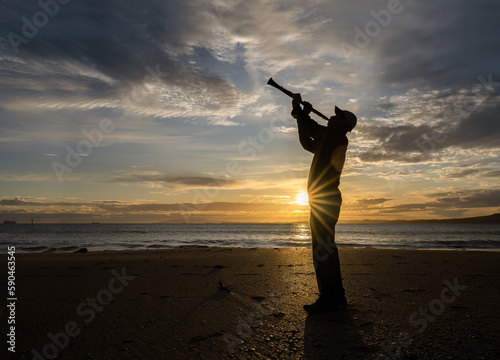 Musician playing Clarinet on a sandy beach at sunrise. Sun starbursts shining through the clouds. Auckland.