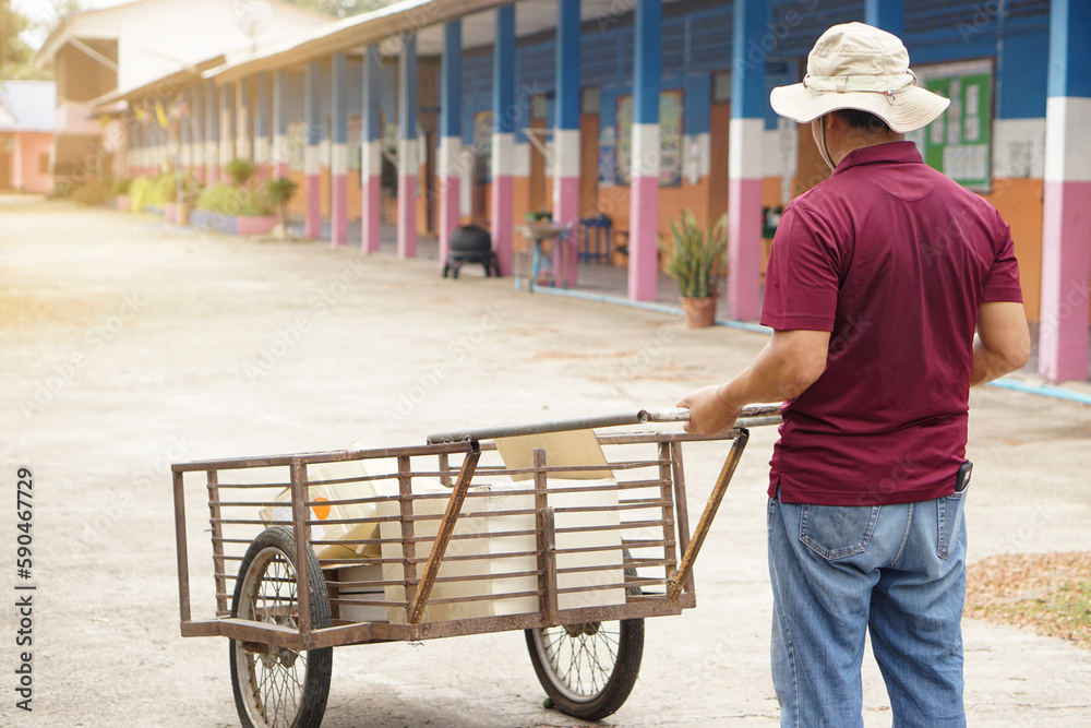 Back view of Asian man janitor is carrying wheel cart to keep garbage in school. Concept, service occupation. Clean keeper for good environment. Collector garbage to recycle. Service man.  