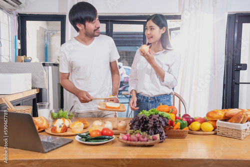 Young Asian couple cooking with fruits and vegetables and using laptop in the kitchen To cook food together within the family happily  family concept.