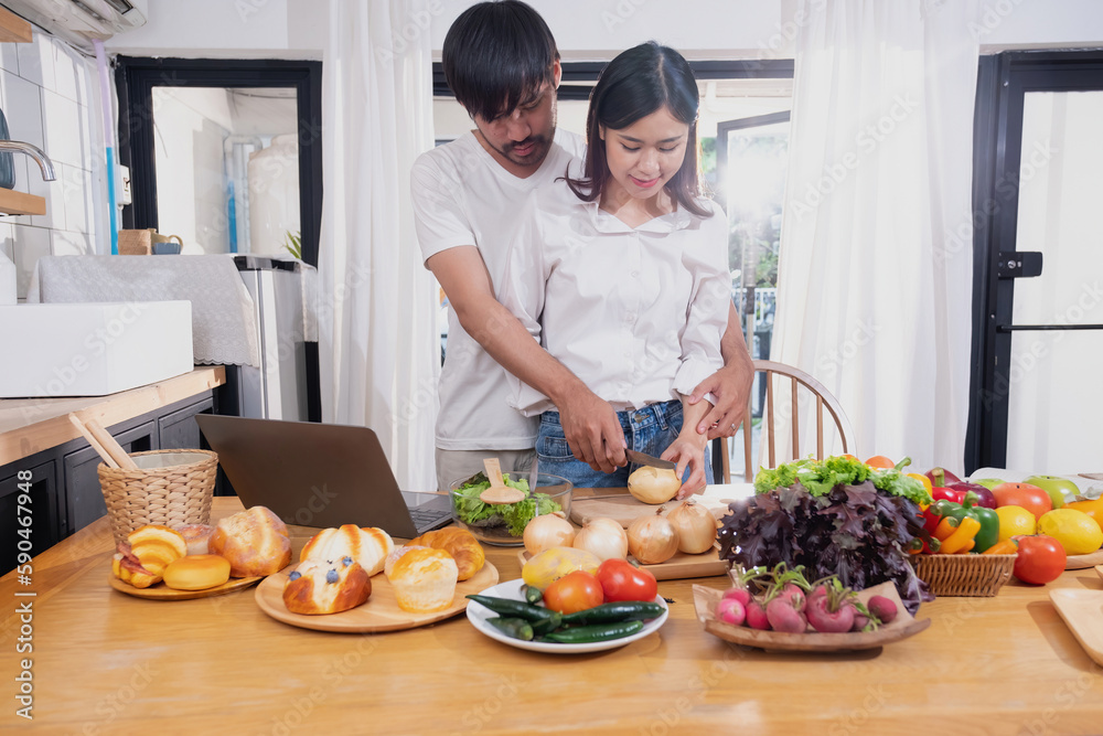 Young Asian couple cooking with fruits and vegetables and using laptop in the kitchen To cook food together within the family happily, family concept. Young Asian couple cooking with fruits and vegetables and using laptop in the kitchen To cook food together within the family happily, family concept.