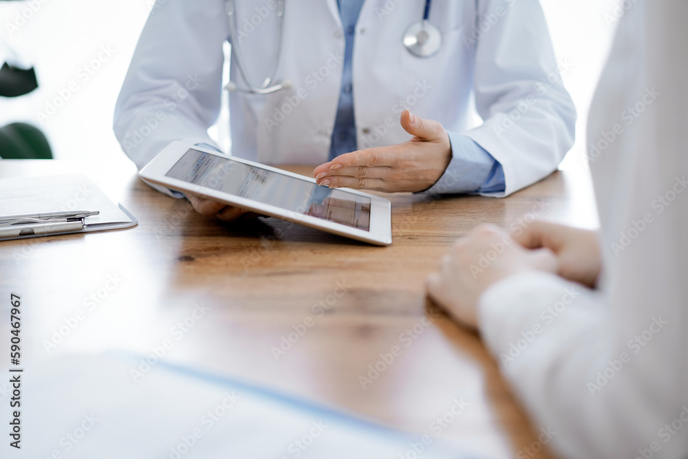 Doctor and patient sitting at the wooden desk in clinic. Female physician's hands pointing into laptop computer monitor, close up. Medicine concept Doctor and patient sitting at the wooden desk in clinic. Female physician's hands pointing into laptop computer monitor, close up. Medicine concept
