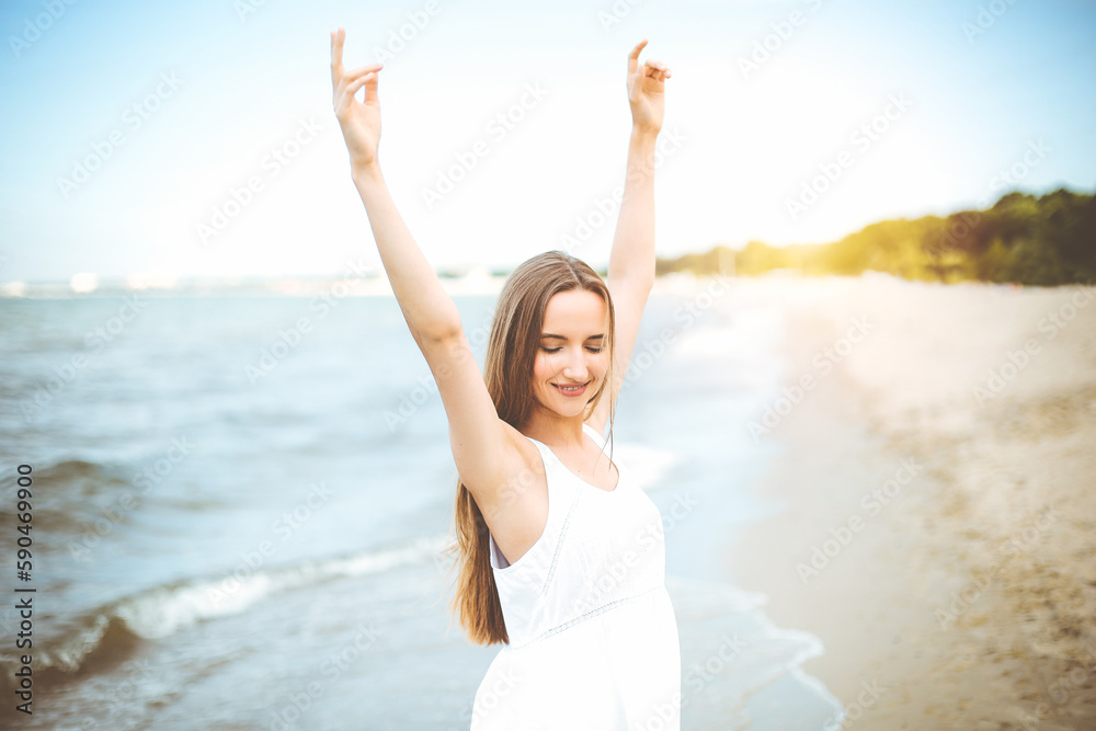 Happy smiling woman in free happiness bliss on ocean beach standing with raising hands. Portrait of a multicultural female model in white summer dress enjoying nature Happy smiling woman in free happiness bliss on ocean beach standing with raising hands. Portrait of a multicultural female model in white summer dress enjoying nature