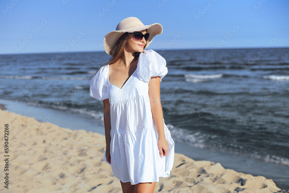 Happy smiling blonde woman is posing on the ocean beach with sunglasses and a hat Happy smiling blonde woman is posing on the ocean beach with sunglasses and a hat