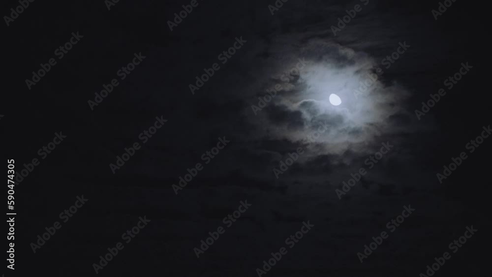 Scenic view of the moon shining between fluffy clouds in the dark sky at nighttime Scenic view of the moon shining between fluffy clouds in the dark sky at nighttime