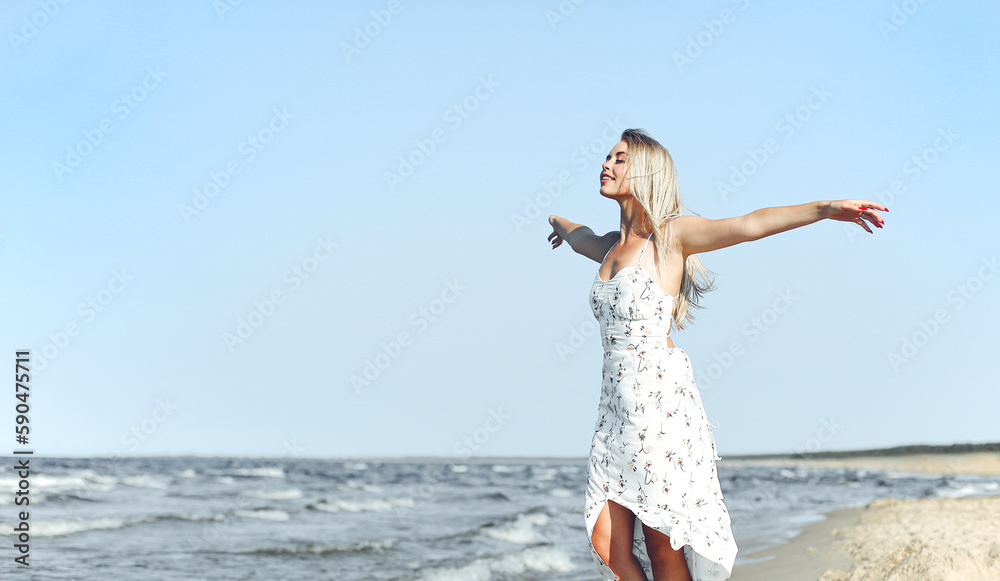 Happy blonde beautiful woman on the ocean beach standing in a white summer dress, open arms Happy blonde beautiful woman on the ocean beach standing in a white summer dress, open arms