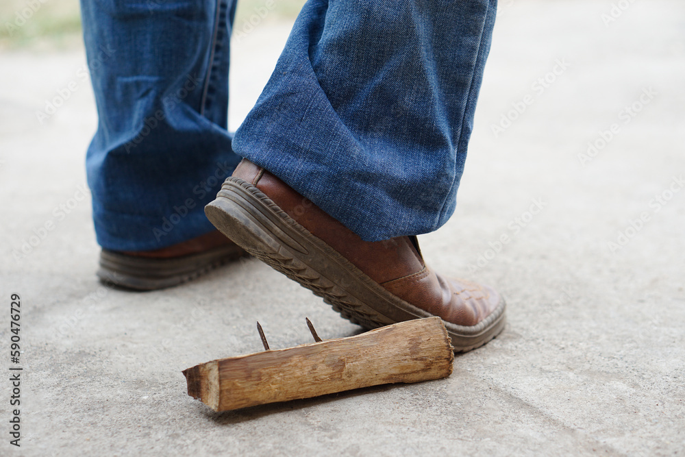 Closeup man wears shoes is stepping on rusty metal nail on wood