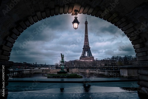 View of the Eiffel Tower from a medieval building's arch on a cloudy day in Paris © Frederic Le Monnier Images/Wirestock Creators