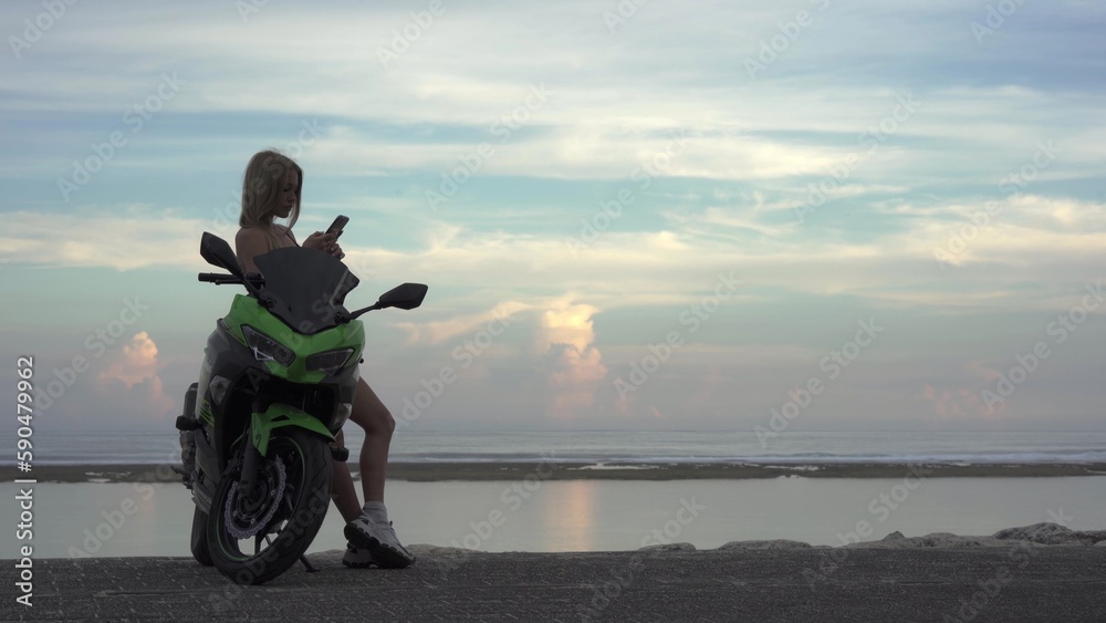 Obraz premium a girl on a motorcycle, looking at her phone, a traveling woman enjoying a ride on a motorcycle, a happy woman, 4k