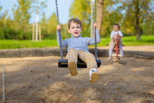 Boy on a swing and girl in the background on a children's playground © michaelheim
