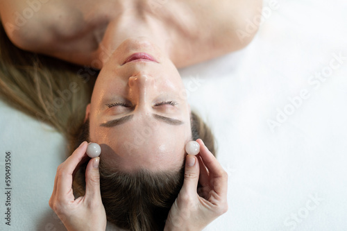 Close-up of the model's face and the masseur's hands. Massage with stone balls. The background is light. Cosmetology. massaging face