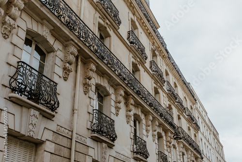 Exterior of aged residential building of beige color with glass windows and beautiful cast iron balconies located in the center of Paris, France