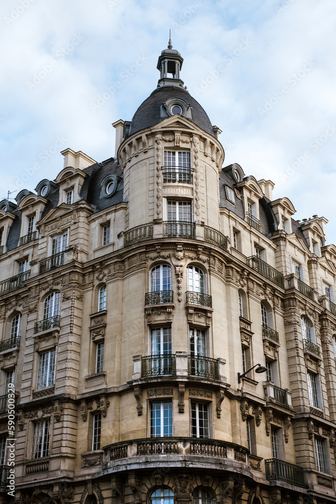 Exterior of aged residential building of beige color with glass windows and beautiful cast iron balconies located in the center of Paris, France