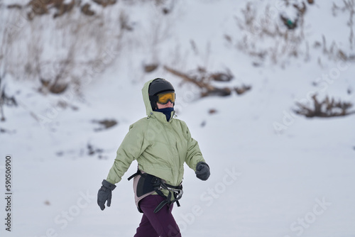 A middle-aged woman, a snowsurfer, walks on the ice of a lake. Preparing to ride a sailboard in the snow on a cloudy winter day.