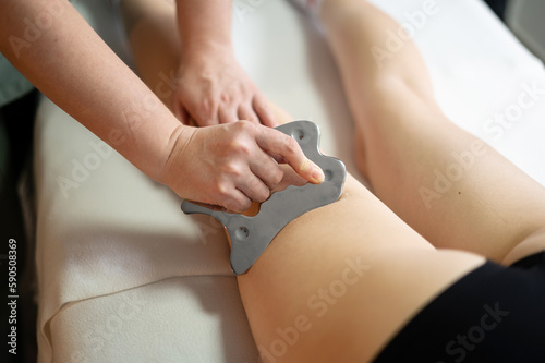 Hands of the masseur are close-up using a metal massage tool to massage the body of a woman lying on a couch. Health concept  body care  skin care  wellness