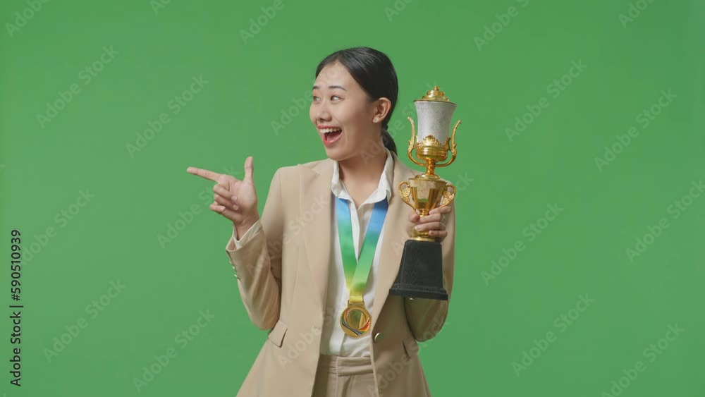 Asian Business Woman In A Suit With A Gold Medal Holding A Gold Trophy In Her Hands, Smiling, And Pointing To Side On Green Screen Background In The Studio
Asian Business Woman In A Suit With A Gold Medal Holding A Gold Trophy In Her Hands, Smiling, And Pointing To Side On Green Screen Background In The Studio