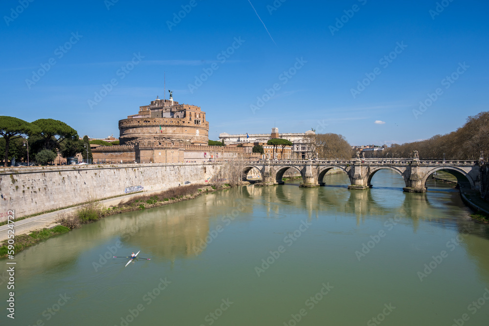 Rom, Italien, Apr. 2023 ein Ruderer auf dem Tiber mit der Ponte Sant Angelo und der Engelsburg im Hintergrund das Gebäude des Cassationsgerichts vor blauem Himmel