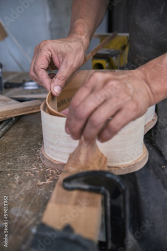 A man's hands gluing the wood of a ukulele under construction.