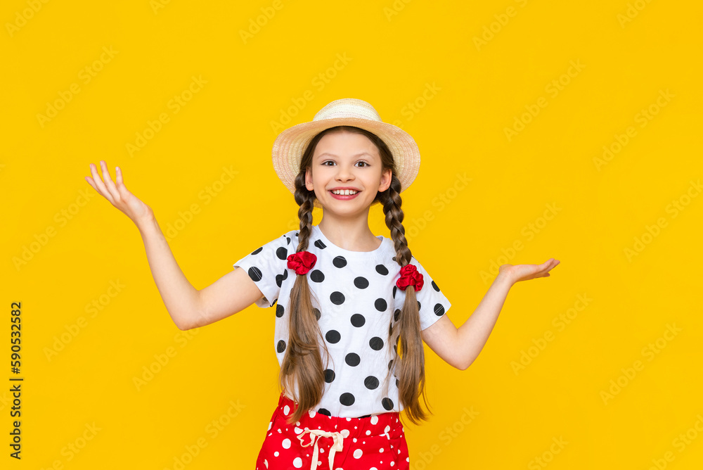 The little girl spread her arms to the sides and points to your advertisement, holding it in the palm of her hand. A beautiful, smiling child in a straw summer hat on a yellow isolated background. The little girl spread her arms to the sides and points to your advertisement, holding it in the palm of her hand. A beautiful, smiling child in a straw summer hat on a yellow isolated background.