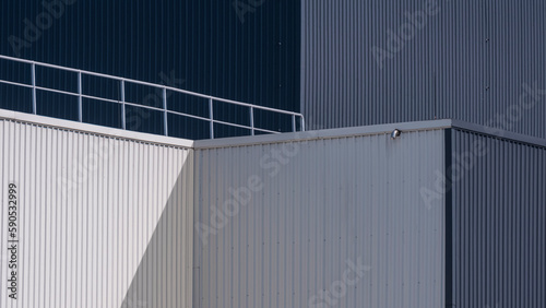 Sunlight and shadow on surface of modern white and gray corrugated metal factory building with steel fence on rooftop in perspective side view