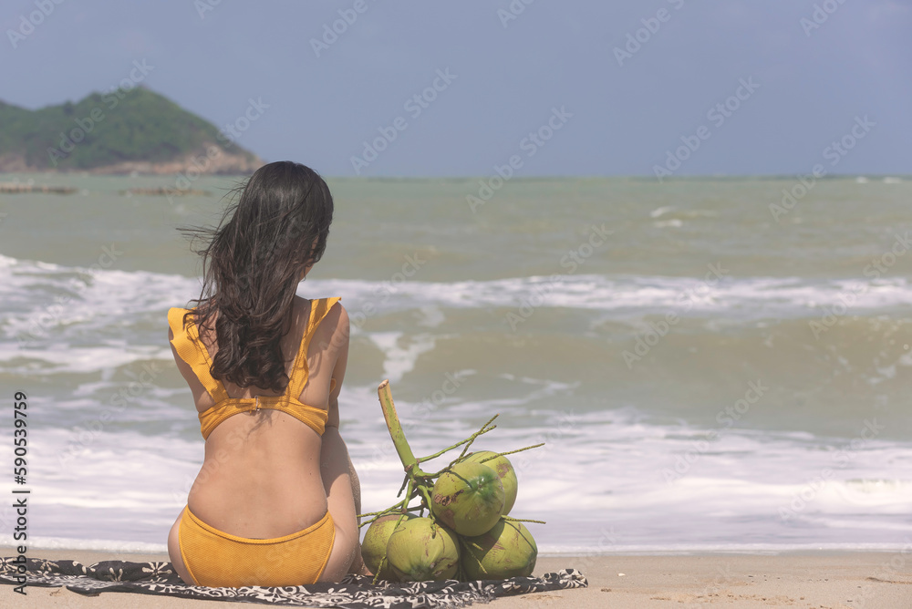 Beautiful woman in swimsuit bikini sitting at the beach by the sea. Wind blow from the sea feel good.