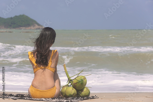 Obraz na płótnie Beautiful woman in swimsuit bikini sitting at the beach by the sea. Wind blow from the sea feel good. w salonie