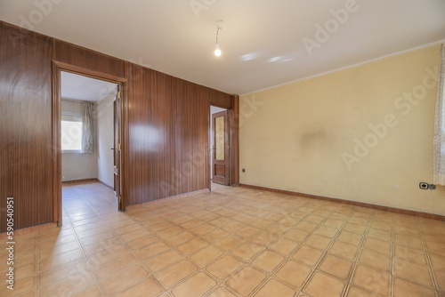 An empty room with poorly painted walls  doors made of sapele wood and a wall covered with the same material and old stoneware floors