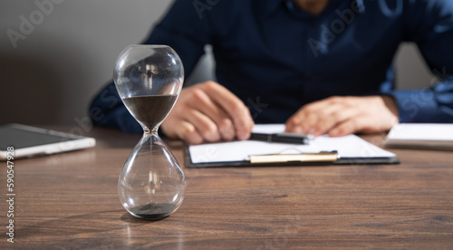Businessman working at office with a hourglass on the table.