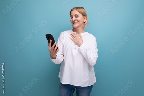pensive slender blondie middle-aged woman in a white blouse masters the smartphone gadget